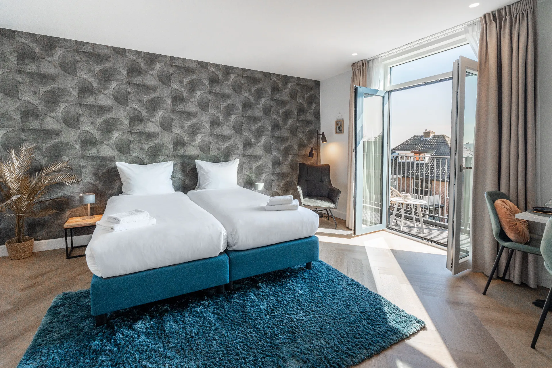 Twin room with balcony at Ocean House Zandvoort, with patterned wallpaper and doors opening onto the balcony
