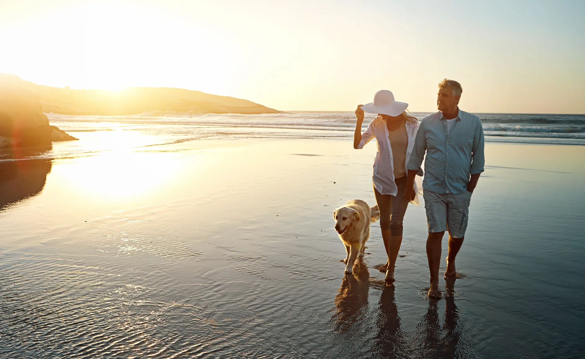 Couple walking their dog along the waterline of Zandvoort beach at golden hour, near Ocean House